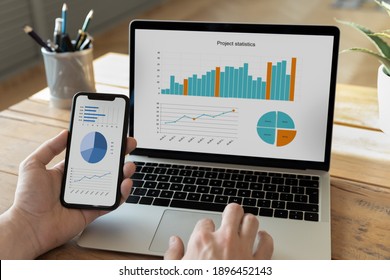 Close up young male ceo executive manager or economist analyzing project statistics using mobile phone and computer applications, developing sales strategy, modern technology gadgets usage at work. - Shutterstock ID 1896452143