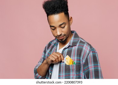 Close up young man of African American ethnicity 20s he wear blue shirt hold in hand mock up of credit bank card put into pocket isolated on plain pastel light pink background People lifestyle concept - Shutterstock ID 2200807393