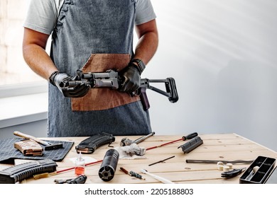 Close up of young man in apron disassembling a gun above the table