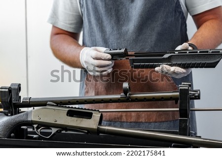 Close up of young man in apron disassembling a gun above the table