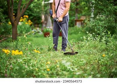 Close up of young man cutting grass with weed cutter on his grassy lawn. Gardening concept
