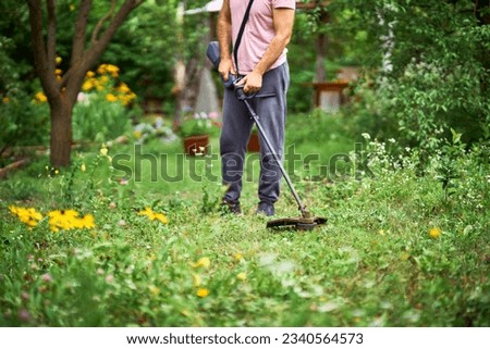 Close up of young man cutting grass with weed cutter on his grassy lawn. Gardening concept
