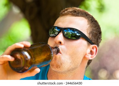 Close Up Of A Young Man Drinking Beer From Bottle Outdoors.