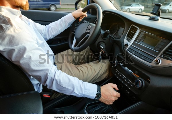 Close up of young man driving expensive car,\
seat belt strapped, hands w/ watch on steering wheel &\
shifting transmission gears, keys in ignition. Businessman rides\
his vehicle. Side view,\
background.