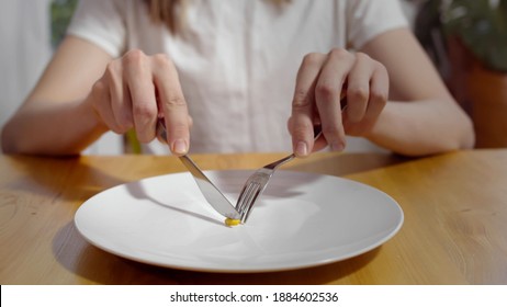 Close Up Of Young Man Eating One Pea With Fork And Knife. Male Sitting At Table And Having Corn Grain For Dinner. Anorexia And Health Problems Concept