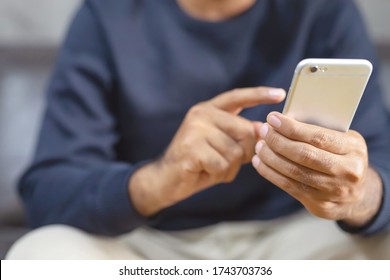 Close Up Young Man Hand Using On Cell Phone During Rest On Sofa Living Room. Sitting In Watching Message On Mobile Smart Phone During Break Relax. Soft Focus.