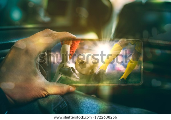 Close up of young man\
hand using a mobile phone to watching football match while sitting\
inside a car