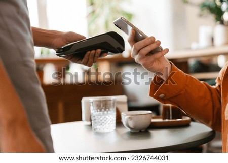 Close up young man paying in cafe with mobile phone using contactless bank terminal