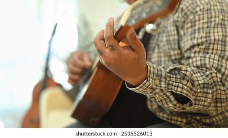 Close up of young man practicing guitar chords in living room - Powered by Shutterstock