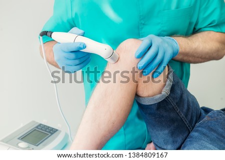 Close up Young man receiving laser or magnet therapy massage on a knee to less pain. A chiropractor treats patient's knee-joint in medical office. Neurology, Osteopathy, chiropractic. Copy space Stock photo © 