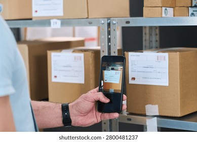 Close up of young man scanning package label with smartphone at order pickup point, managing inventory and delivery workflow. Useful for logistics, ecommerce, fulfillment marketing