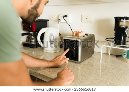 Close up of a young man smiling while putting bread in the toaster while preparing breakfast in the morning while at the kitchen