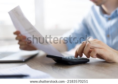 Close up young man using calculator, managing household monthly budget, summarizing taxes or bills, planning future investments, doing financial affairs at home, accounting bookkeeping concept.
