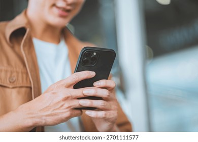 Close up of young man using smartphone, male hands holding mobile phone while texting or browsing online, modern digital lifestyle concept with communication technology and casual outfit in urban sett