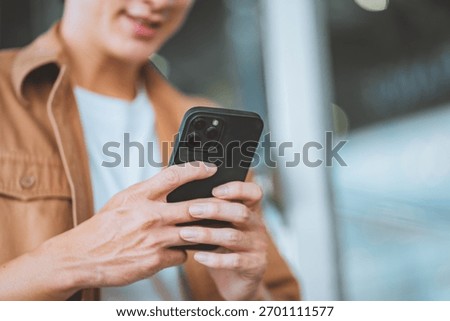 Close up of young man using smartphone, male hands holding mobile phone while texting or browsing online, modern digital lifestyle concept with communication technology and casual outfit in urban sett