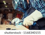 Close up of a young  man welder in  uniform, welding mask and welders leathers, weld  metal  with a arc welding machine  in workshop, blue and orange  sparks fly to the sides