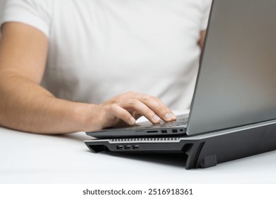 Close up of young man working on laptop on a cooling stand