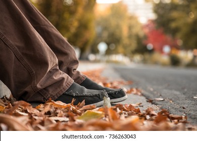 Close Up Of Young Mans Feet In Autumn Leaves on Ground By Curb In City Street. Selective Focus Bokeh Background With Copy Space. - Powered by Shutterstock
