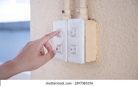 Close Up Young Man's Hand Pressed The Button To Turn On The Light Switch, Open The Electrical Circuit Beside The Wall.