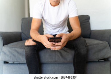 Close up of a young mans hand using on cell phone while sitting on the sofa in the living room.