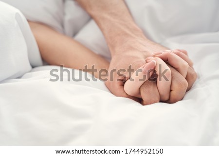 Close up of a young married couple holding hands during the moment of intimacy in bed