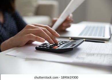 Close up young mixed race woman calculating domestic expenses involved in financial paperwork indoors, focused lady managing monthly banking payments summarizing utility bills and taxes at home.