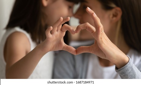 Close up of young mother and cute little daughter make heart sign with hands enjoy close tender moment together, caring mom and grateful small girl child show love and support in family relationships