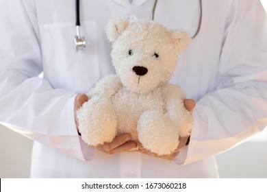 Close Up Young Pediatrician In White Coat Holding Toy In Hands, Showing Professional Friendly Attitude To Children. General Practitioner Demonstrating Stress Free Doctor Visit, Healthcare Concept.