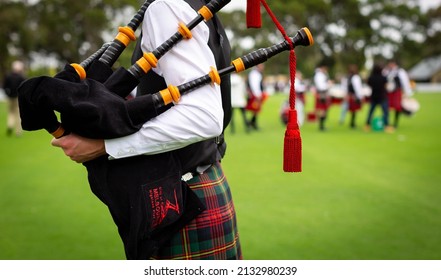 Close Up Of Young Person Holding Scots Bagpipes With Band In Distance.