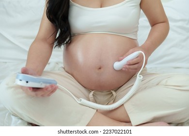 close up young pregnant woman using fetal droppler device to listening baby heartbeat - Shutterstock ID 2237022101