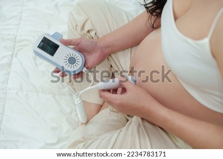 close up young pregnant woman using fetal droppler device to listening baby heartbeat