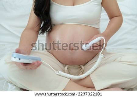 close up young pregnant woman using fetal droppler device to listening baby heartbeat