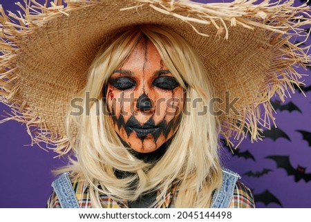 Close up young scary woman with Halloween makeup mask in straw hat scarecrow costume stand with closed eyes isolated on plain dark purple background studio portrait Celebration holiday party concept.