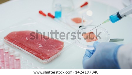 Close up of an young scientist is inspecting and analyzing with syringe the cultured artificial meat sample in laboratory.