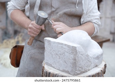 Close up of young sculptor hands working on his marble sculpture in his workshop with hammer and chisel