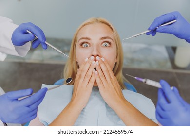 Close Up Young Shocked Scared Frightened Woman Covered By Blue Napkin Cover Mouth With Arm Look At Doctor Hand Hold Instruments Sit At Dental Office Chair Indoor Cabinet Being Afraid Of Oral Procedure