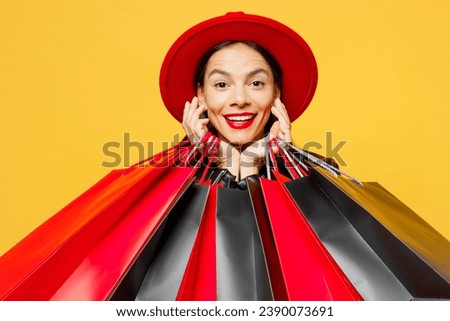 Close up young smiling cheerful fun happy woman wearing casual clothes red hat holding shopping paper package bags looking camera isolated on plain yellow background. Black Friday sale buy day concept