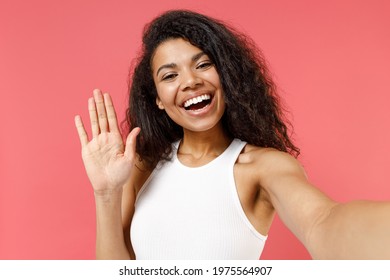 Close up young smiling friendly african american woman 20s in casual white tank shirt do selfie shot on mobile phone talk by video call waving hand greeting isolated on pink background studio portrait - Powered by Shutterstock