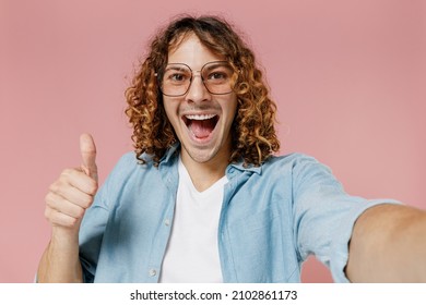 Close Up Young Smiling Happy Man 20s With Long Curly Hair Wear Blue Shirt White T-shirt Glasses Do Selfie Shot Pov On Mobile Phone Show Thumb Up Isolated On Pastel Plain Pink Color Background Studio