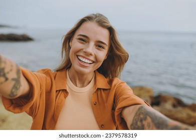 Close up young smiling happy woman she wears orange shirt casual clothes doing selfie shot pov on mobile cell phone walk on sea ocean sand shore beach outdoor seaside in summer day. Lifestyle concept - Powered by Shutterstock