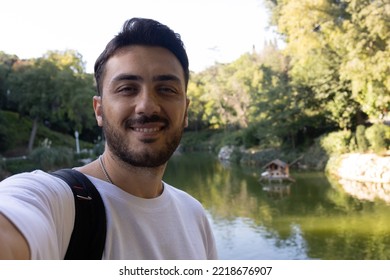 Close Up Young Smiling Man In Casual Clothes Posing With Lake. People Sincere Emotions Lifestyle Concept. Mock Up Copy Space. Doing Selfie Shot On Mobile Phone.