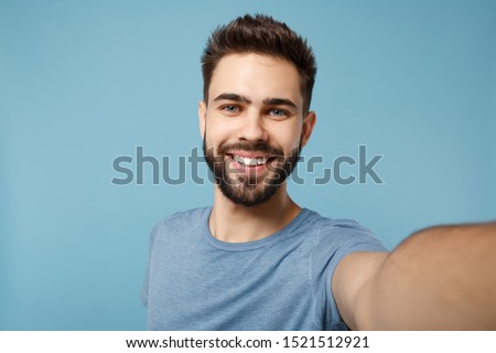 Close up Young smiling man in casual clothes posing isolated on blue wall background, studio portrait. People sincere emotions lifestyle concept. Mock up copy space. Doing selfie shot on mobile phone