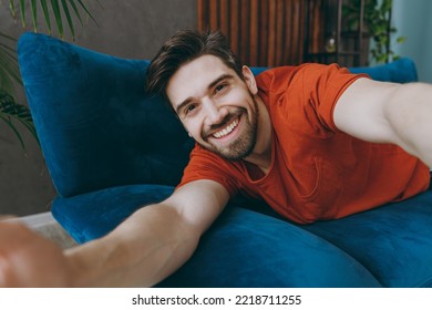 Close Up Young Smiling Man Wear Red T-shirt Do Selfie Shot Pov On Mobile Cell Phone Lay Down Blue Sofa Stay At Home Hotel Flat Rest Spend Free Spare Time In Living Room Indoors People Lounge Concept