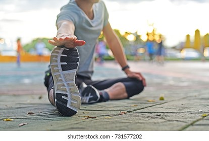 Close up young sport man is stretching leg muscle to prevent injury before exercise or running, good performance, flexibility, warm up, in morning time with sunrise at city park