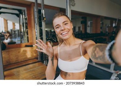 Close up young sporty athletic sportswoman woman in white sportswear warm up training sit near treadmill trainers do selfie shot on mobile cell phone wave hand in gym indoors Workout sport concept. - Powered by Shutterstock