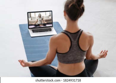 Close up of young sporty woman practicing yoga online with laptop at home. Yoga instructor conducting video training via video conference. Meditation, Sukhasana, relax. Healthy lifestyle concept