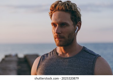 Close up young strong sporty athletic toned fit sportsman man in sports clothes earphones warm up training with music at sunrise sun dawn over sea beach outdoor on pier seaside in summer day morning.