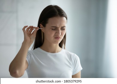 Close up young woman cleaning ears, using cotton bud after shower, feeling pain, beautiful female wearing white t-shirt standing in bathroom, morning routine, personal hygiene concept - Shutterstock ID 1805379295