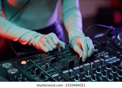 Close up young woman as DJ making music tracks at mixer table in neon light - Shutterstock ID 2310484021