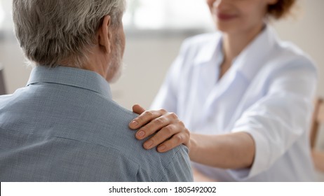 Close up young woman doctor touching senior patient shoulder at meeting in hospital, caring physician gp comforting and supporting mature man at medical appointment, psychological help concept - Shutterstock ID 1805492002